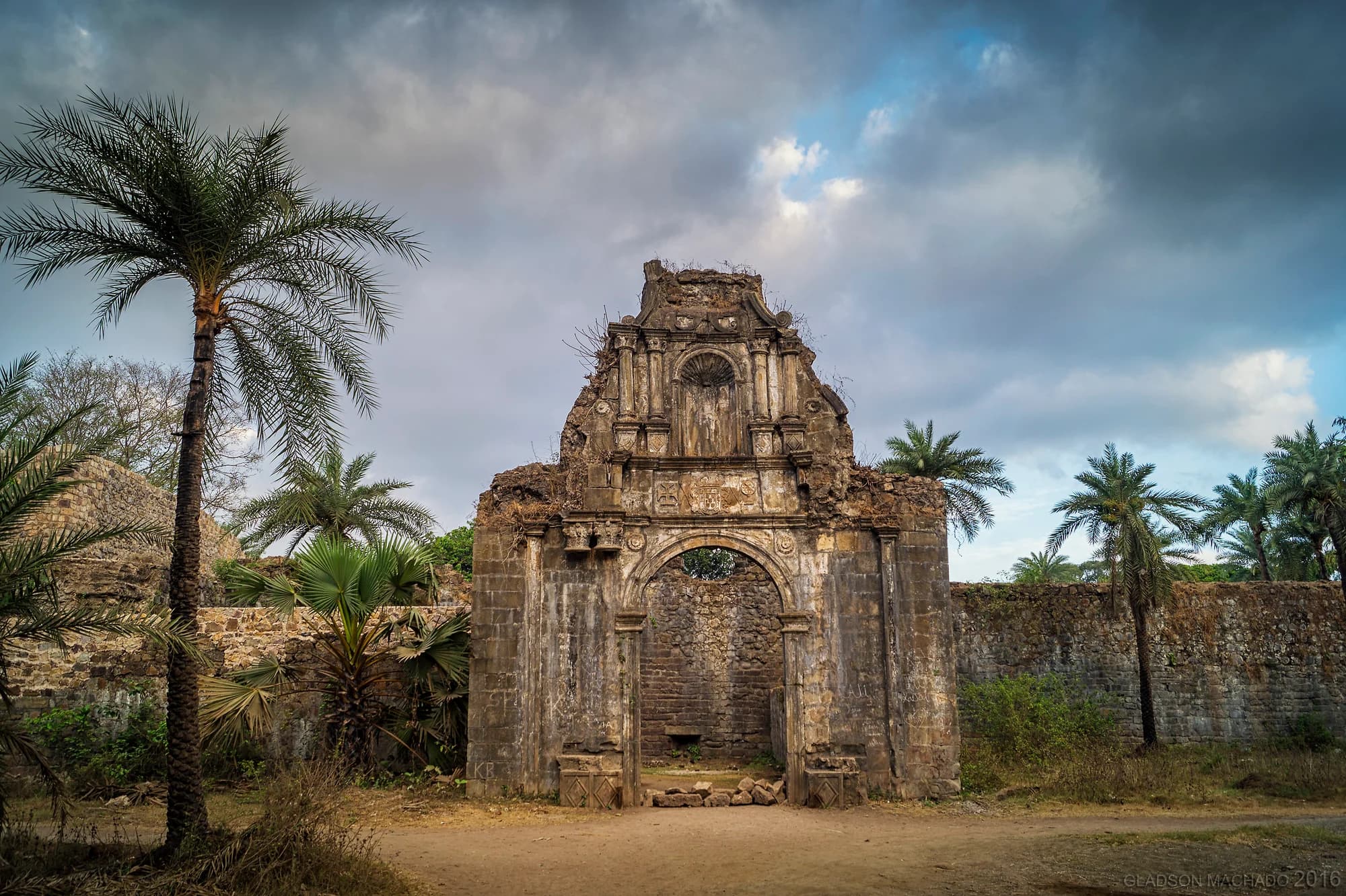A historic stone arch and fort walls surrounded by palms